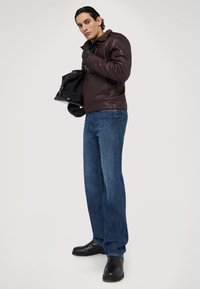 Chaqueta de cuero marrón, jeans azules, guantes negros y botas negras. La chaqueta tiene un cuello y cremallera frontal, con un diseño elegante y ajustado.