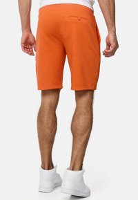 Orange bomuldsshorts med sidelommer og en baglomme med knap, der har en afslappet pasform og færdigsyede kanter. Sammen med hvide sneakers.