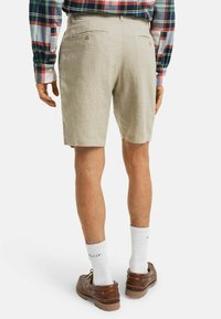 Helle beige Leinen-Shorts mit einer lässigen Passform, die zwei Gesäßtaschen und eine glatte Textur aufweisen. Getragen mit braunen Bootsschuhen und weißen Socken.