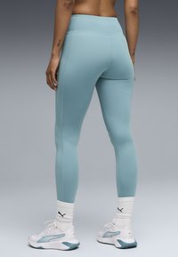 Ένα ζευγάρι ανοιχτό μπλε αθλητικό κολάν κατασκευασμένο από λείο, ελαστικό ύφασμα, με ψηλή μέση και ραφές flatlock. Φορεμένο με λευκά αθλητικά παπούτσια.