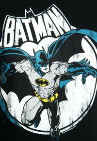 Black T-shirt featuring a graphic of Batman in blue and white, with a yellow emblem. The design is bold, showing dynamic action and detail.