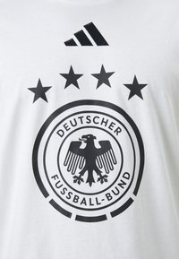Hvit bomulls-T-skjorte med et svart tysk fotballforbundslogo med en dobbel sirkel, en ørn og fire svarte stjerner over.