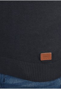 Marine gebreide trui met ribbelmanchetten en -zoom. Bruin leren label met een reliëfinscriptie op de taille. Geen zichtbare patronen of accenten.