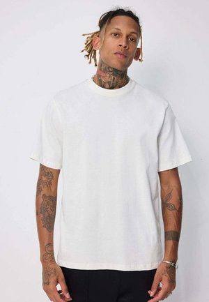 T-shirt en coton blanc avec un col rond, des manches courtes et une coupe décontractée. Texture lisse, sans motifs ni ornements.