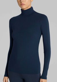 Maglia a collo alto navy realizzata in tessuto liscio e elastico. Maniche lunghe con un design aderente e un colletto alto discreto. Dettagli delle cuciture sull'orlo.
