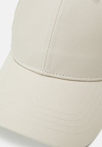 Beige baseball cap featuring a structured crown, a curved brim, ribbed texture, and contrasting white stitching on the seams.