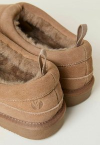 Brown suede slip-on shoes with soft fur lining, textured rubber outsole, and small fabric loops at the back for easy wear.