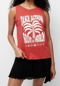 Rød ærmeløs tanktop med hvidt tekstgrafik og palmetrædesign, kombineret med en sort mini-nederdel med tekstur og bølget kant.