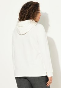 Felpa bianca con cappuccio, maniche lunghe, vestibilità comoda, caratterizzata da yoke posteriore e spacco laterale, abbinata a pantaloni grigi con motivo.