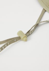 Bežinė virvė su plastikiniu reguliatoriumi, turinti lygią, blizgią tekstūrą. Ant virvės ilgio yra užrašas "Jordan" baltos spalvos.