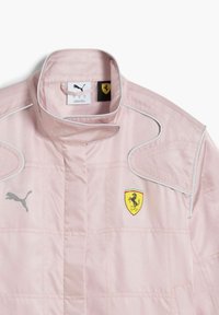 Lichtroze jack met zilveren piping, voorzien van een Puma-logo en een geel Ferrari-embleem. Gemaakt van textuurstof met een hoge kraagontwerp.