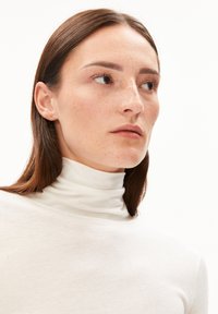 Witte coltrui gemaakt van een lichtgewicht stof, met een aansluitend ontwerp en een gladde textuur, nauwsluitend bij de nek.