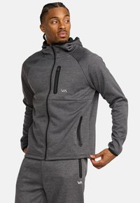 Veste zippée grise en tissu doux, dotée d'une capuche ajustée, de poches zippées à l'avant et d'un logo sur la poitrine. Texture lisse, design athlétique.