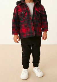 Röd och svart rutigt flanelljacka med huva, framdragkedja, två bröstfickor; parat med svarta mjukisbyxor och vita sneakers.