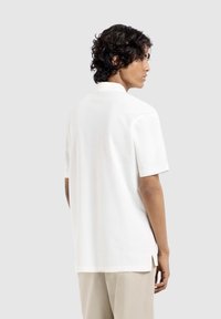 Korte mouwen, wit polo shirt met een rechte snit, zachte textuur en zijsplitten. Het heeft een klassieke kraag en minimale details.