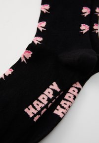 Fekete zoknik rózsaszín balettcipő mintákkal és a csuklón olvasható "HAPPY" felirattal, vastag betűtípussal. Sima, rugalmas anyag.