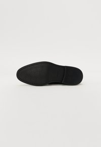 Talpă de pantof neagră din cauciuc texturat, având un model circular. Forma este plată, cu vârful rotunjit și branding subtil.