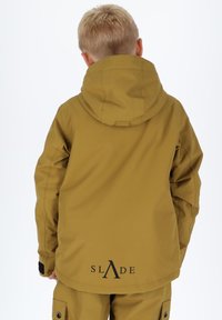 Gelbe wasserdichte Jacke mit Kapuze, mit einem Logo auf dem Rücken. Glatte Textur und lockere Passform, kombiniert mit passenden Hosen.
