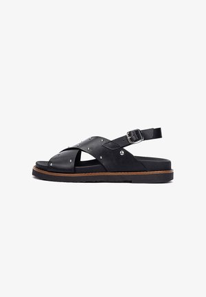 Sandalo in pelle nera con borchie argento, cinturini incrociati, fibbia regolabile alla caviglia e piattaforma con suola piatta marrone.