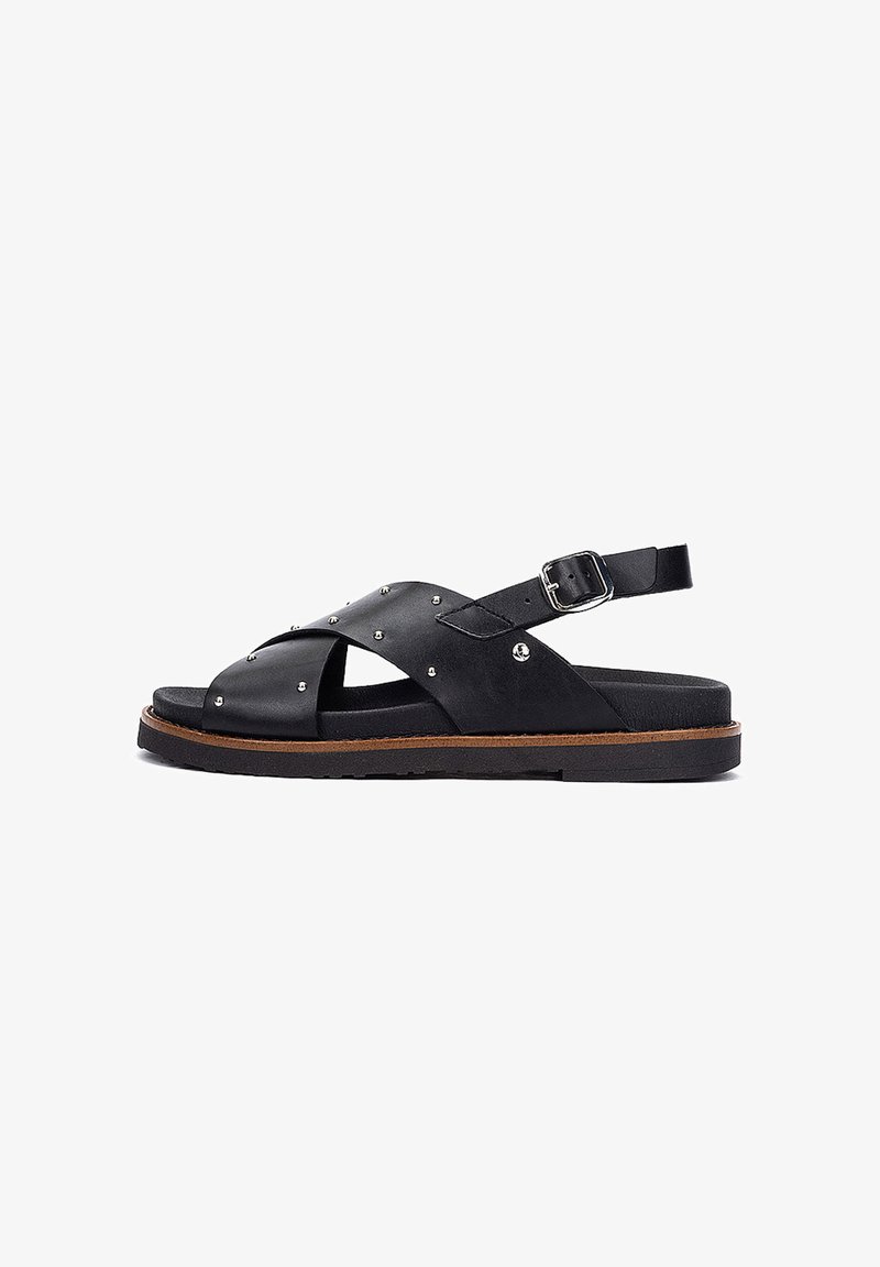 Sandalo in pelle nera con borchie argento, cinturini incrociati, fibbia regolabile alla caviglia e piattaforma con suola piatta marrone.