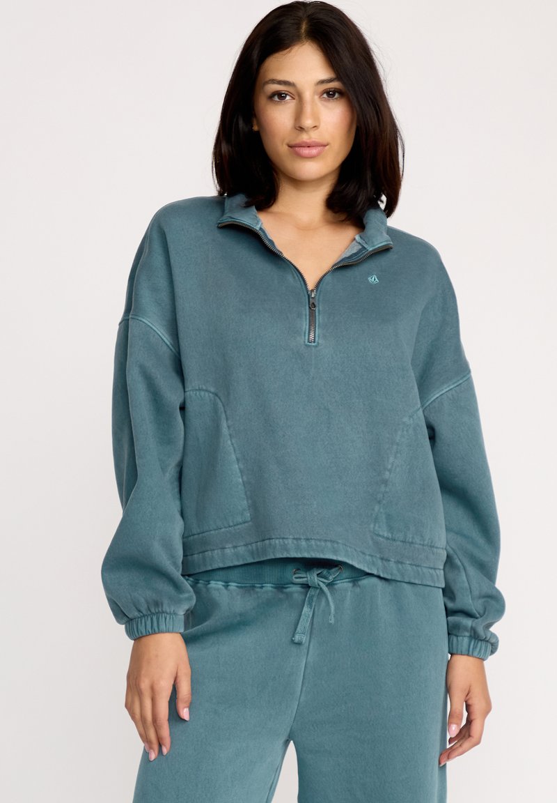 Teal pullover sweatshirt, cropped design, halvdels-lynlås foran, ribbede manchetter, børstet tekstur, med et lille logo på brystet.