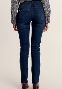 Schmale, dunkelblaue Jeans mit mittelhohem Bund, ausgestattet mit zwei Gesäßtaschen und kontrastierenden Nähten, kombiniert mit einer gemusterten Bluse.