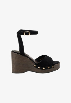 Sandalia cuña de ante negro con plataforma de madera, correa en el tobillo con hebilla dorada, puntera abierta y tachuelas doradas a lo largo del borde de la suela.