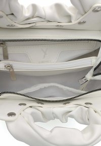 Balta somiņa ar maigu, sakratu dizainu. Iekšpusē ir kabata ar rāvējslēdzēju un sudraba toņu detaļas aizvēršanai. virsma gluda visā.