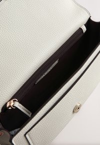 Petit sac en cuir blanc texturé ouvert pour montrer une poche zippée noire à l’intérieur et une fermeture aimantée sur le rabat avant.