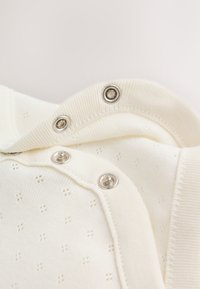 Close-up of white fabric with small diamond patterns featuring silver-colored snap fasteners along a ribbed edge.