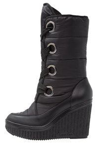 Botas negras de cuña con una parte superior textil acolchada. Cuentan con grandes ojales de metal, cierre con cordones en la parte delantera y suela plataforma de goma texturizada.