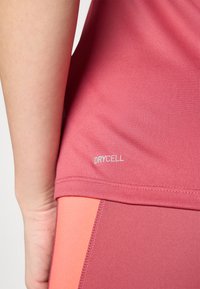 Roosa sporditop, millel on "DRYCELL" silt, sile tekstuur ja kehakujuline disain, mille alumises osas on oranžid aktsentpaneelid.