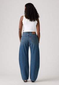 Jeans de ganga de perna larga em azul médio, com uma cintura alta, costura clássica, dois bolsos traseiros e um patch de logo em pele na cintura.