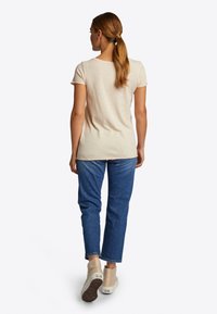 Beige T-Shirt mit kurzen Ärmeln und Rundhalsausschnitt, kombiniert mit blauen geraden Jeans. Das Outfit wird mit beigen Sneakers abgerundet.