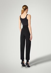 Sort tætsiddende top kombineret med sorte bukser med høj talje, elastisk talje og tilspidsede manchetter, afsluttet med sorte højhælede sko.