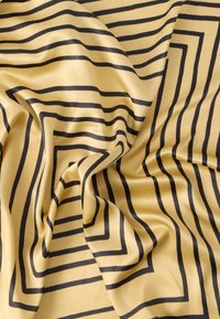 Λείος χρυσός ύφασμα με μαύρα ομόκεντρα τετράγωνα σχέδια, ελαφρώς τσαλακωμένο και σα σερβιέτα.