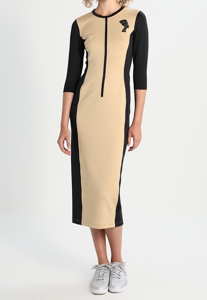Robe longue beige et noire avec des manches 3/4, fermeture éclair devant et panneaux latéraux ; elle présente un accent graphique de profil sur la poitrine.