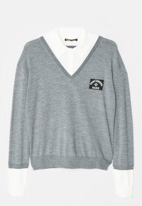 Grijze V-hals trui gedragen over een wit overhemd met kraag, met een patch "Saint Honore Paris" op de borst en witte manchetten.