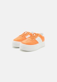 Baskets orange avec des accents blancs, présentant une tige lisse, un design à lacets et une semelle blanche épaisse et texturée.