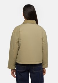 Giacca khaki con colletto in corduroy, texture imbottita e silhouette corta; presenta tasche laterali e maniche ampie.