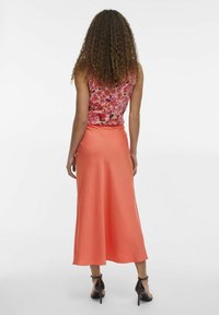 Rosa blommig ärmlös topp i kombination med en korallfärgad satin midi-kjol, som har en slät textur och en flödande design. Svarta klackskor med ankelsnodd.