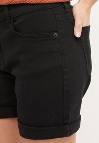 Shorts en denim noir avec des revers, dotés d'une poche frontale, d'une texture lisse et de coutures soignées.