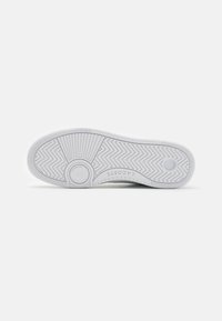 Hvit sneakersåle med teksturert mønster, sirkulære detaljer og logo. Glatt materiale med sikksakk-grep for godt feste.