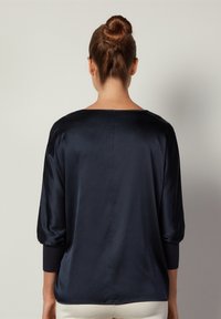 Haut en satin marine avec des manches trois-quarts, un col large et une texture lisse. Dispose d'une couture arrière droite et de poignets ajustés.