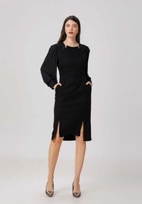 Robe noire avec de longues manches bouffantes, dotée d'une fente sur les côtés, de poches et d'une silhouette ajustée. Texture lisse, design jusqu'au genou.