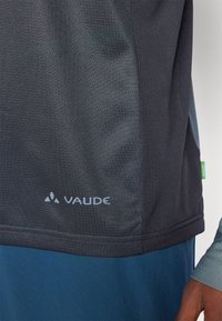 Sötétszürke légáteresztő sportpóló, hálós textúrával, világosszürke "VAUDE" logóval és kék kiegészítőkkel. A varrások részletezve vannak.