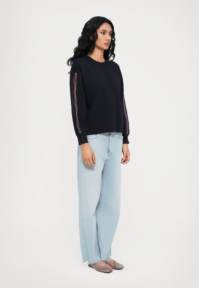 Navy blue knit sweater with long sleeves, featuring a multi-colored stripe along the outer sleeves. Paired with light blue wide-leg jeans.