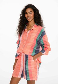 Košeľa s krátkym rukávom, s gombíkmi a zodpovedajúcou sukňou v koralovej, zelenej a námorníckej pruhovanej vzore. Ľahká látka s voľným strihom a vreckami.