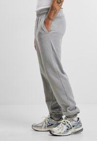 Gray sweatpants with elastic waistband and side pockets, featuring a relaxed fit and ribbed cuffs. Paired with silver athletic sneakers.