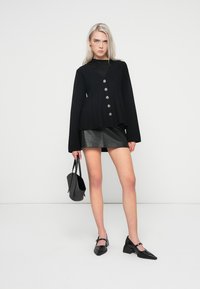 Top tricotat negru cu decolteu în V și cinci butoane decorative, asociat cu o fustă mini din piele neagră, ajustată, cu un model de crocodil.